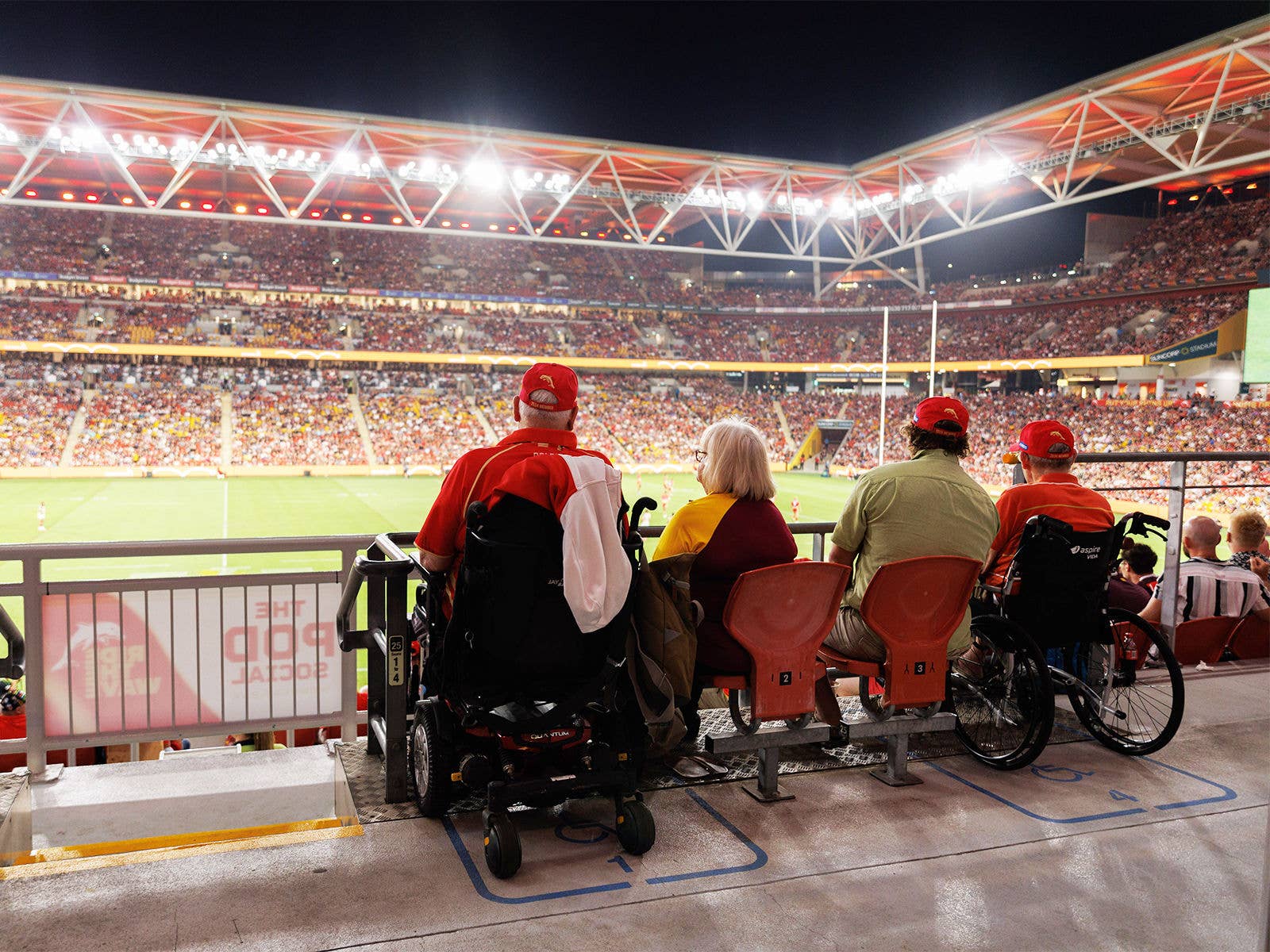 Accessibility Four patrons sat in the Accessible seating area at Suncorp Stadium watching a nighttime game.